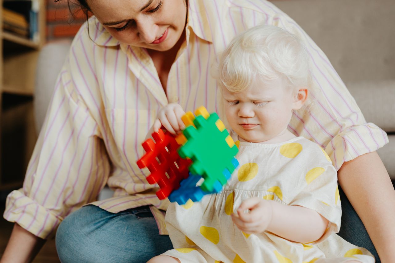 A mother and her albino child enjoy playing with colorful puzzle blocks indoors.